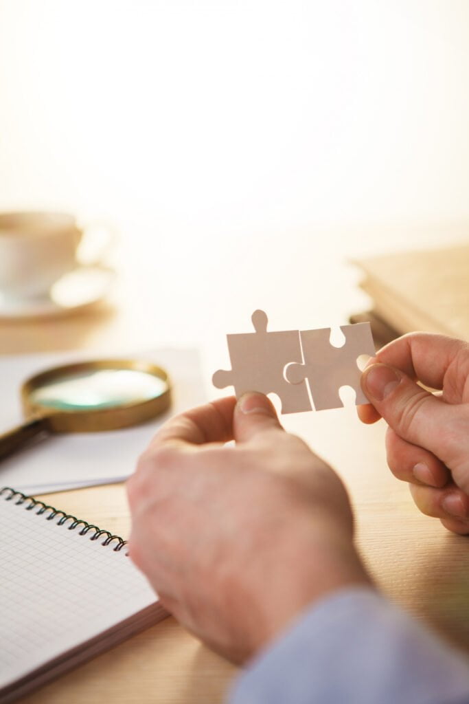 Hands connecting puzzle pieces on desk near coffee